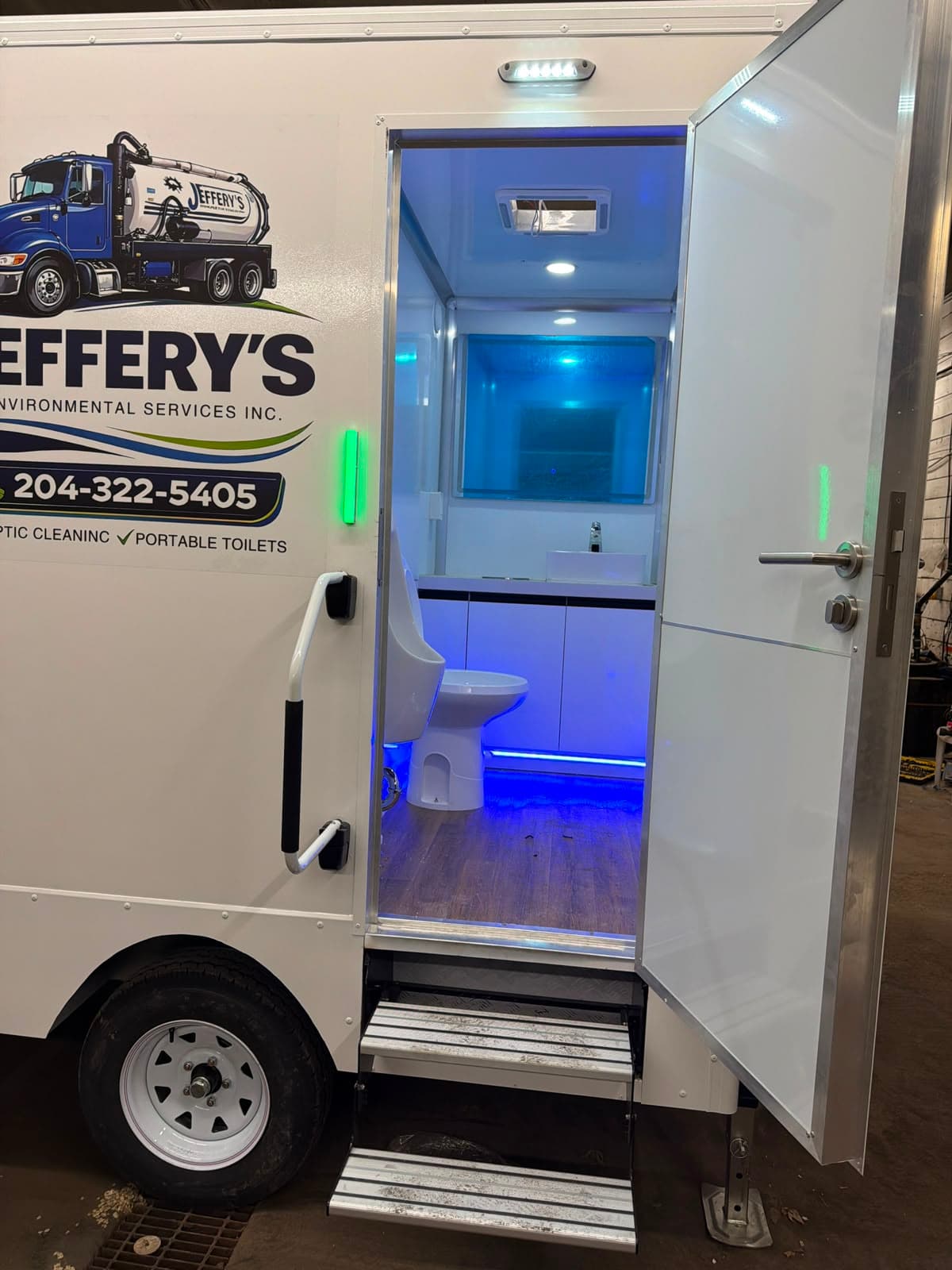 Illuminated interior of Jeffery's luxury restroom trailer with a flushing toilet and handwashing sink